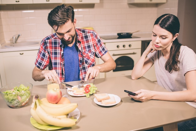 Gelukkig man zit en tafel en eet omlet. Hij snijdt voedsel in stukken met mes en vork. Meisje kijkt naar telefoon die ze in handen houdt. Ze verveelt zich en is moe.
