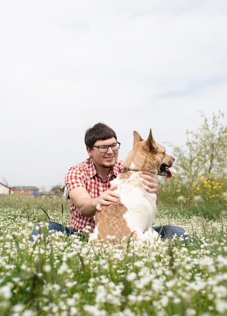 Gelukkig man zit met gemengd ras herdershond op groen gras in Lentebloemen