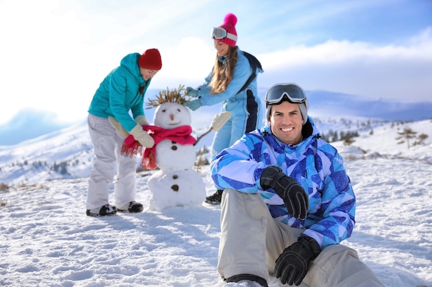 Gelukkig man zit op besneeuwde heuvel in skigebied. Winter vakantie