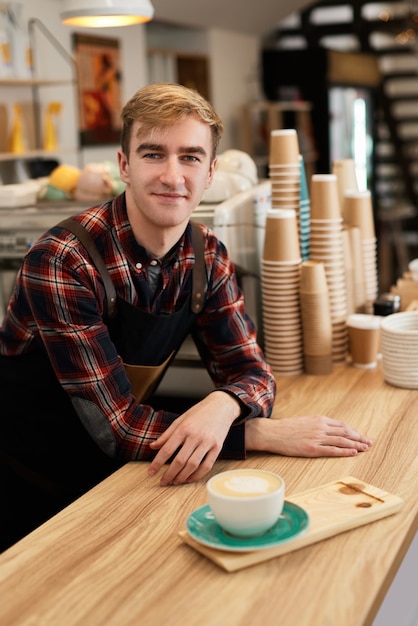 Gelukkig mannelijke ober in schort met kopje warme drank in coffeeshop, barista werkt graag in de cafetaria