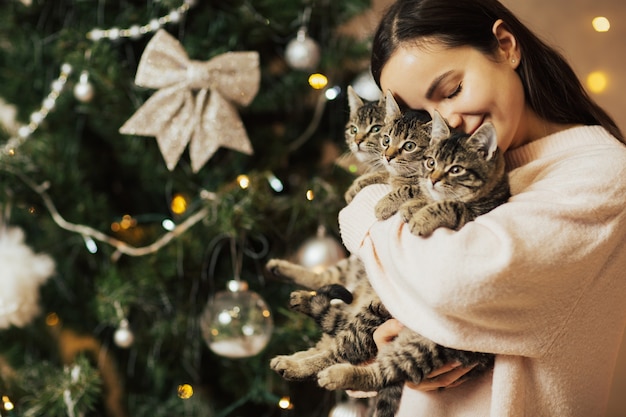 Gelukkig meisje dat drie lieve kittens houdt in de buurt van de kerstboom