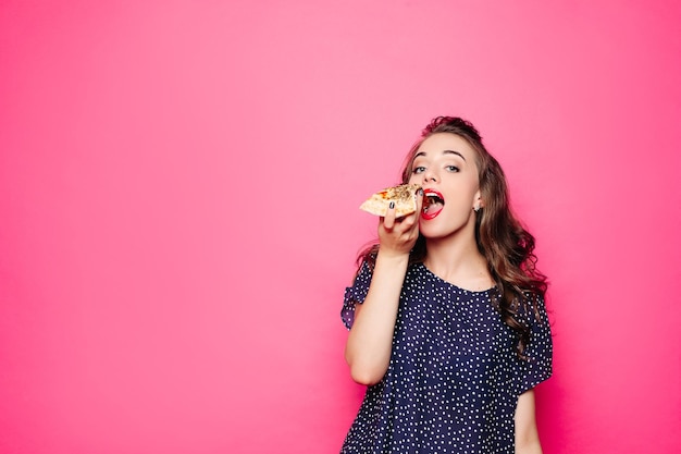 Gelukkig meisje dat een pizza eet Ze opende haar mond met een pizza in haar rechterhand en staarde je tevreden aan Geïsoleerd op roze achtergrond