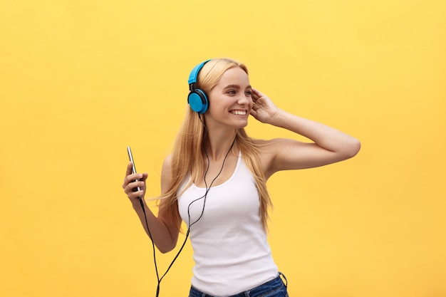 Gelukkig meisje dat en aan de muziek danst luistert die op een gele achtergrond wordt geïsoleerd