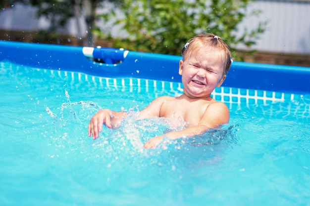 Gelukkig meisje dat in rood zwempak thuis in openlucht zwembad springt. Babymeisje dat leert te zwemmen. Waterplezier voor kinderen.