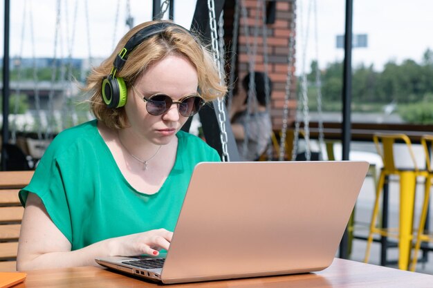 Gelukkig meisje dat op laptop bladert en naar muziek luistert op een koptelefoon in een straatcafé