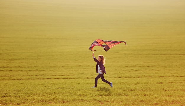 Gelukkig meisje die met vlieger in handen op het mooie gebied lopen