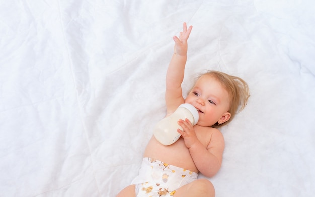 Gelukkig meisje drinkt melk uit een fles terwijl ze op het bed ligt