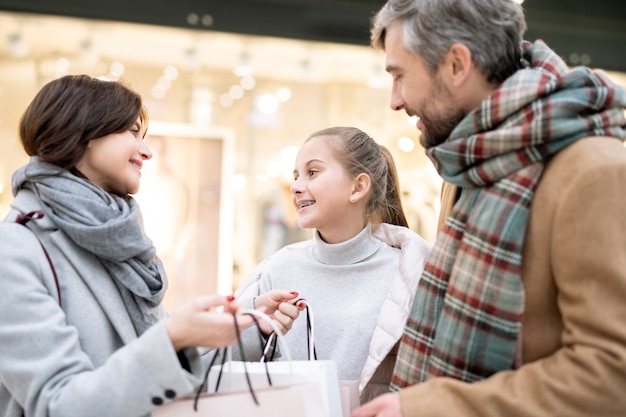 Gelukkig meisje en haar moeder die met papieren zakken naar elkaar kijken terwijl ze bespreken wat ze na het winkelen hebben gekocht