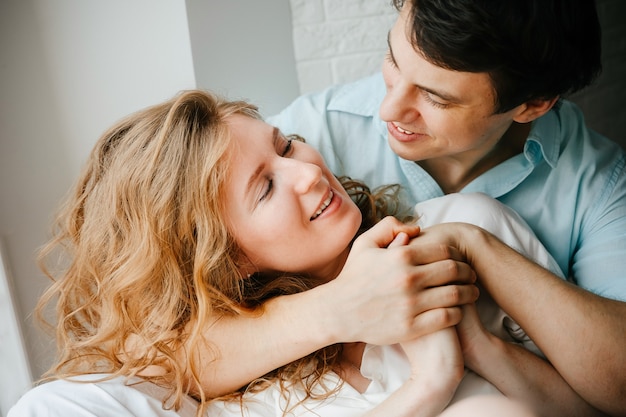 Gelukkig meisje en man knuffelen in de buurt van raam in huis. Witte en blauwe kleding. Valentijnsdag.