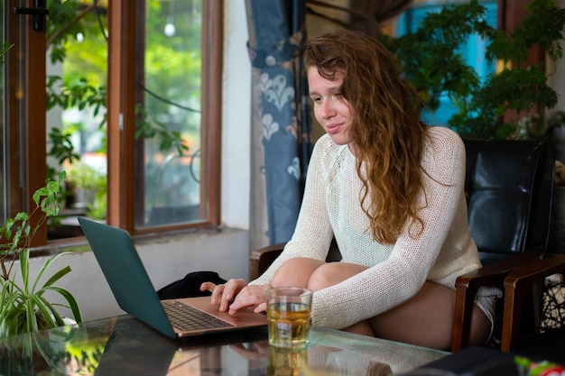 Gelukkig meisje freelancer glimlachend en werkend op een laptop in een groen café of coworking en het drinken van haar drankje