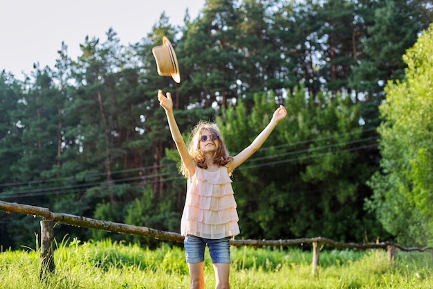 Gelukkig meisje genieten van zomervakantie, kind in de natuur op groene weide spelen met hoed, gooit een hoed naar de hemel