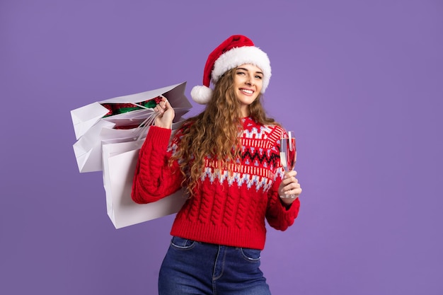 Gelukkig meisje houdt boodschappentassen en champagne op paarse achtergrond kerstverkoop zwarte vrijdag