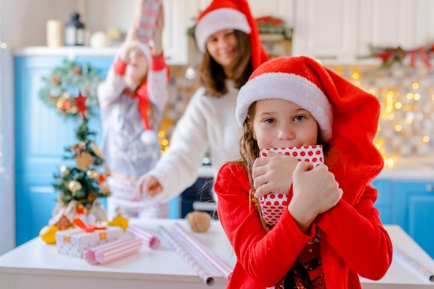 Gelukkig meisje houdt een cadeau vast, moeder en zus hebben plezier op de achtergrond in de keuken