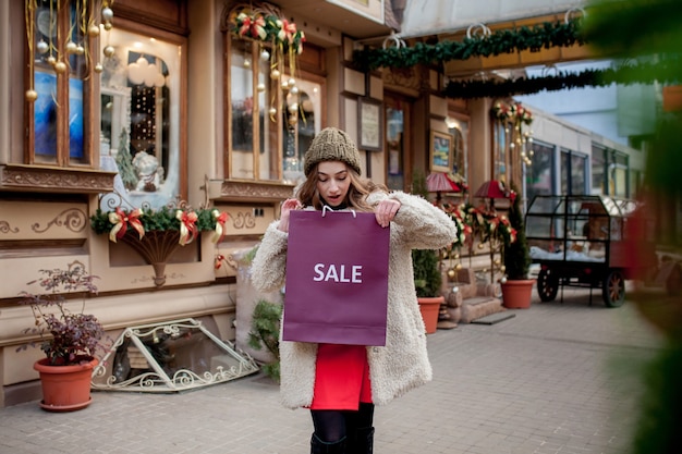 Gelukkig meisje houdt paperbags met symbool van verkoop in de winkels met verkoop met Kerstmis, rond de stad. Concept van winkelen, vakantie, geluk, kerstverkoop.