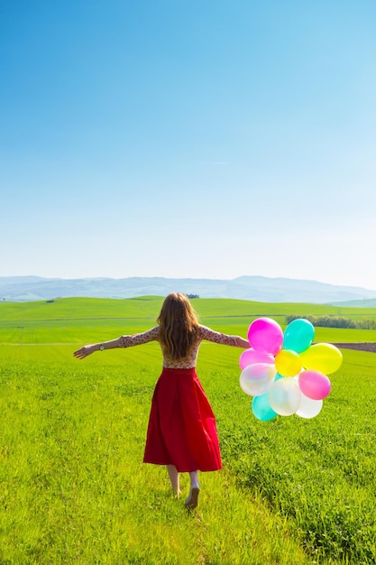 Gelukkig meisje in de toscaanse weiden met kleurrijke ballonnen, tegen de blauwe lucht en de groene weide. toscane, italië