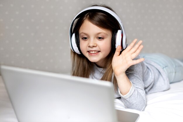 Gelukkig meisje in draadloze koptelefoon communiceert vreugdevol via internet op een laptopcomputer
