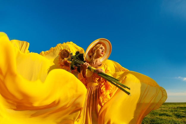 gelukkig meisje in een gele jurk houdt zonnebloembloemen in een veld met zonnebloemen tegen de lucht