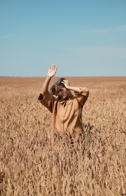 Foto gelukkig meisje in een hoed die danst in een veld op een heldere blauwe hemelachtergrond