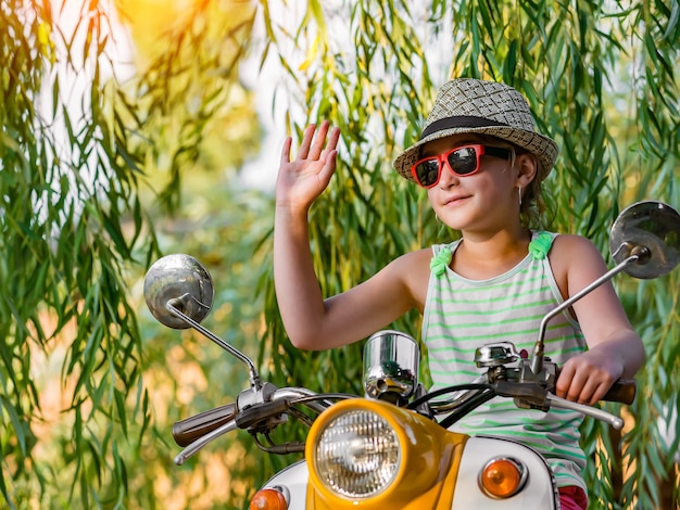 Gelukkig meisje in een hoed en zonnebril op een scooter