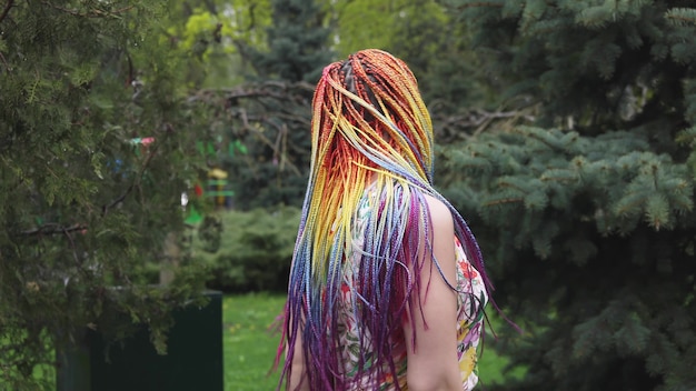 Gelukkig meisje in een jurk met regenboog Afrikaanse vlechten en heldere kleurrijke make-up. schattig lacht en gooit haar haar in de lucht en dwarrelt tijdens een wandeling in het lentepark