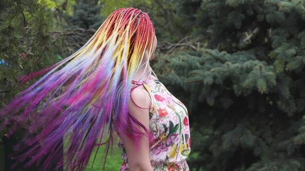 Gelukkig meisje in een jurk met regenboog Afrikaanse vlechten en heldere kleurrijke make-up. schattig lacht en gooit haar haar in de lucht en dwarrelt tijdens een wandeling in het lentepark