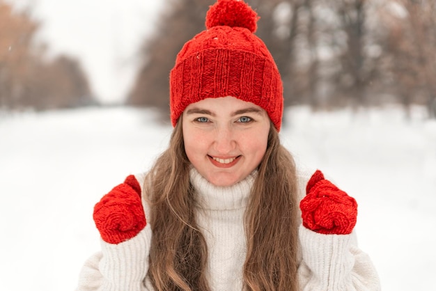 Gelukkig meisje in gebreide sweaterrode muts en wanten in winterpark Vrouw warmt op in wollen kleding buitenkoud weer