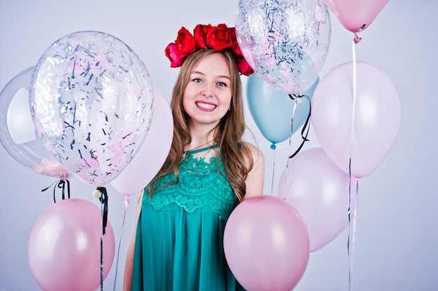 Gelukkig meisje in groene turkooise kleding en kroon met gekleurde ballons die op wit worden geïsoleerd. Vieren verjaardagsthema.