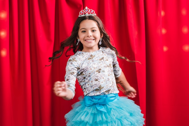 Gelukkig meisje in leuke kleding die voor rood gordijn danst