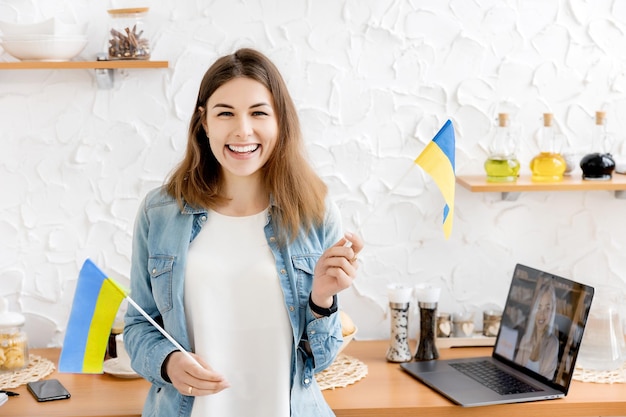 Gelukkig meisje kijkt naar de camera met de vlag van Oekraïne in haar keuken Spot de oorlogsvrede in Oekraïne