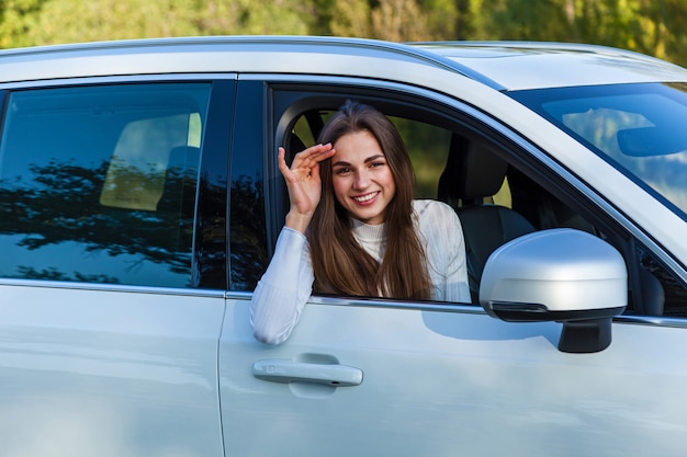 Gelukkig meisje kijkt uit het raam van een witte auto en glimlacht