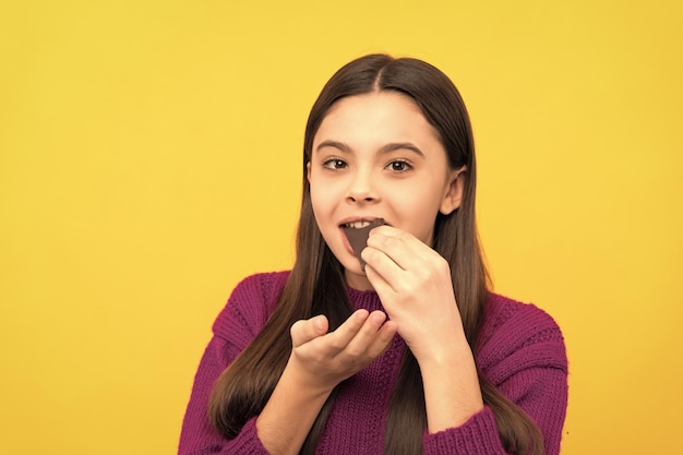 Gelukkig meisje kind bijten chocolade snack gele achtergrond heerlijk