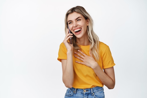 Gelukkig meisje lachen op telefoongesprek, praten met iemand en vrolijk glimlachen, staande in gele tshirt op wit. Mobiel begrip.