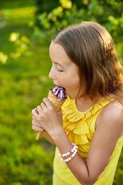 Gelukkig meisje met bretels die Italiaans ijsje eet en glimlacht terwijl ze op zomerdag in het park rust