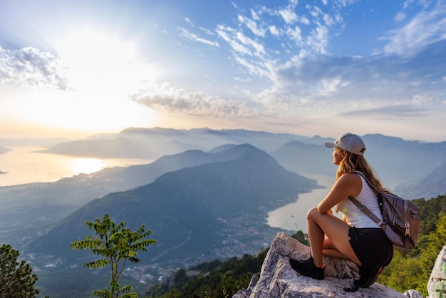 Gelukkig meisje met een rugzak staat aan de rand van een hoge berg in montenegro