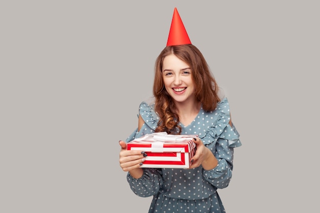 Gelukkig meisje met grappige feestmuts die naar de camera kijkt, een geschenkdoos vasthoudt en glimlacht terwijl ze geniet van verjaardag