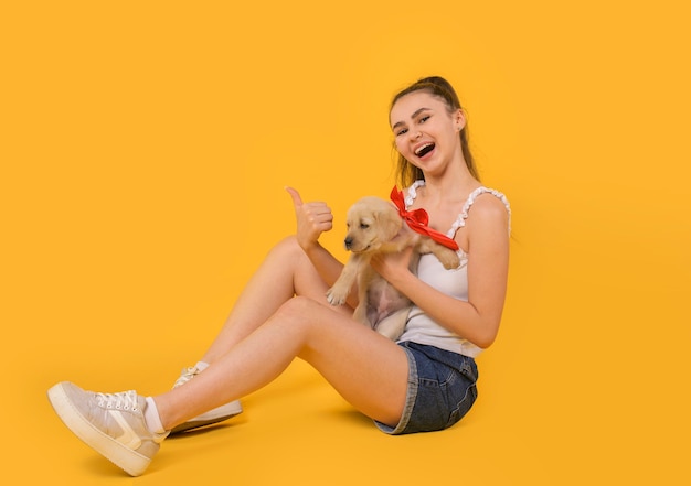 Gelukkig meisje met haar schattige puppy zittend op de vloer op een gele achtergrond