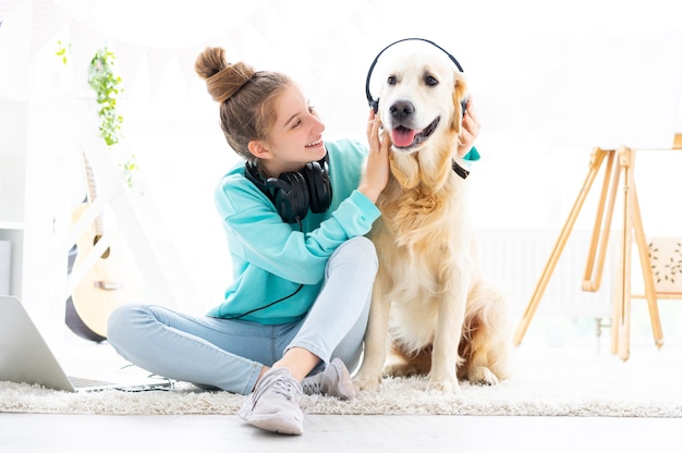 Gelukkig meisje met koptelefoon op het hoofd van de hond zittend op de vloer in lichte kamer