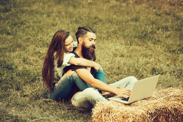 Gelukkig meisje met lachend gezicht heeft lang haar omhelzing bebaarde man hipster werken op laptop op hooi op groen gras buiten