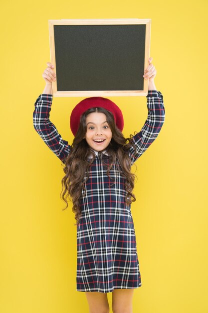 Gelukkig meisje met lang krullend haar in baret kind met leeg schoolbord Parijse kind op gele kopie ruimte promotie klein meisje in frans baret bord voor promotie promotie-informatie