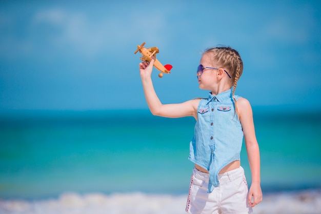 Gelukkig meisje met speelgoed vliegtuig in handen op wit zandstrand. Kind spelen met speelgoed op het strand