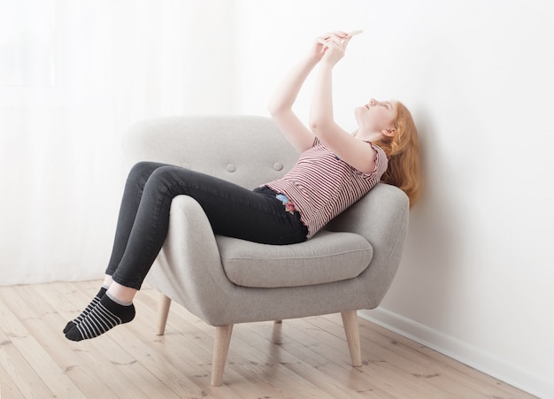 Gelukkig meisje met telefoon in fauteuil