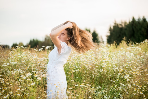 Gelukkig meisje op het veld kamille, zomer zonsondergang. in een witte jurk. rennen en draaien, de wind in mijn haar, levensstijl. vrijheid concept en hete zomer.