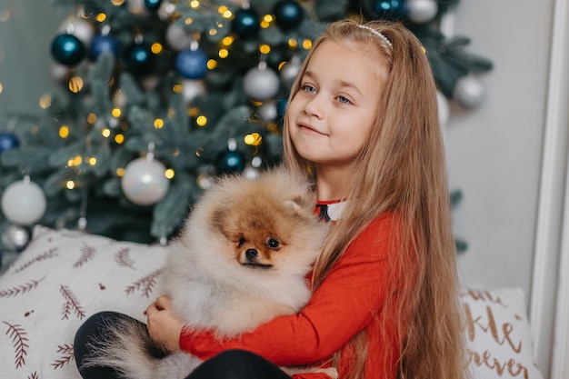 Gelukkig meisje poseren met schattige puppy, kerstboom op de achtergrond, langverwachte pluizig cadeau, joy