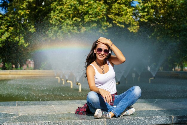 Gelukkig meisje poseren tegen achtergrond fontein op zonnige dag in casual kleding