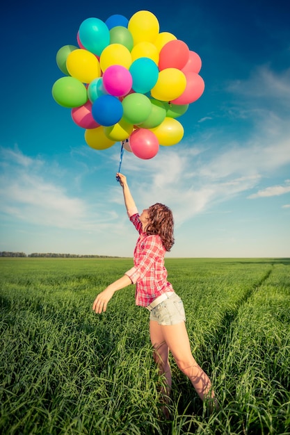 Gelukkig meisje spelen met kleurrijke speelgoed ballonnen buitenshuis Jonge vrouw plezier in groene lente veld tegen blauwe hemelachtergrond Vrijheid concept