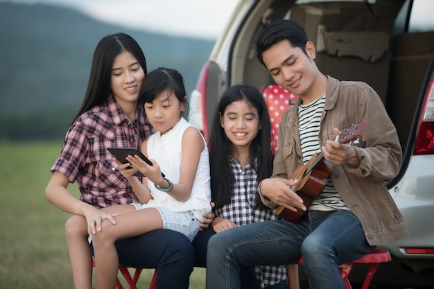 gelukkig meisje spelen ukulele met Aziatische familie zitten in de auto om te genieten van road trip en su