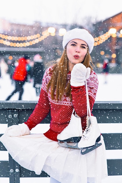 Gelukkig meisje stuurt een luchtkus romantische vrouw vrouw met winter kunstschaatsen op haar schouder win...