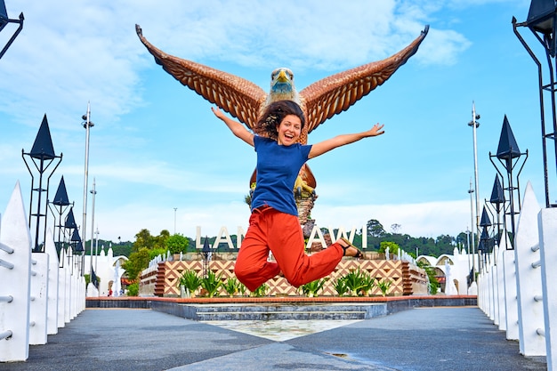 Gelukkig meisje toeristische poseren naast sculptuur van een rode adelaar die zijn vleugels uitspreidt. Populaire toeristische plek op het eiland Langkawi