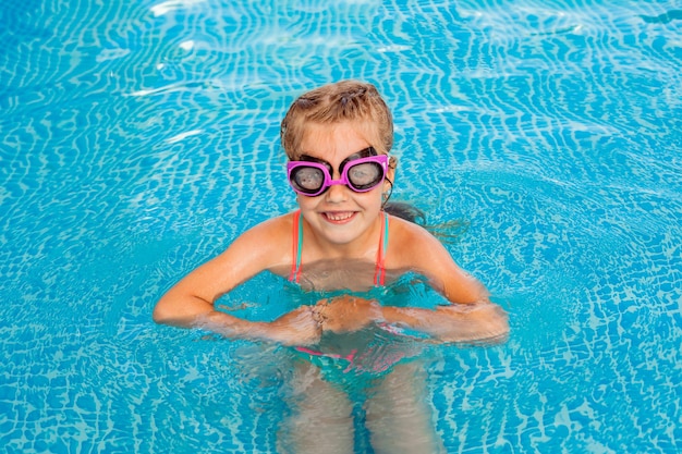 Gelukkig meisje zwemt in het zwembad. zomervakantie. meisje in een zwembroek en zwembril.