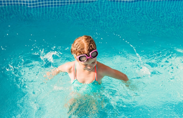 Gelukkig meisje zwemt in het zwembad. zomervakantie. meisje in een zwembroek en zwembril.